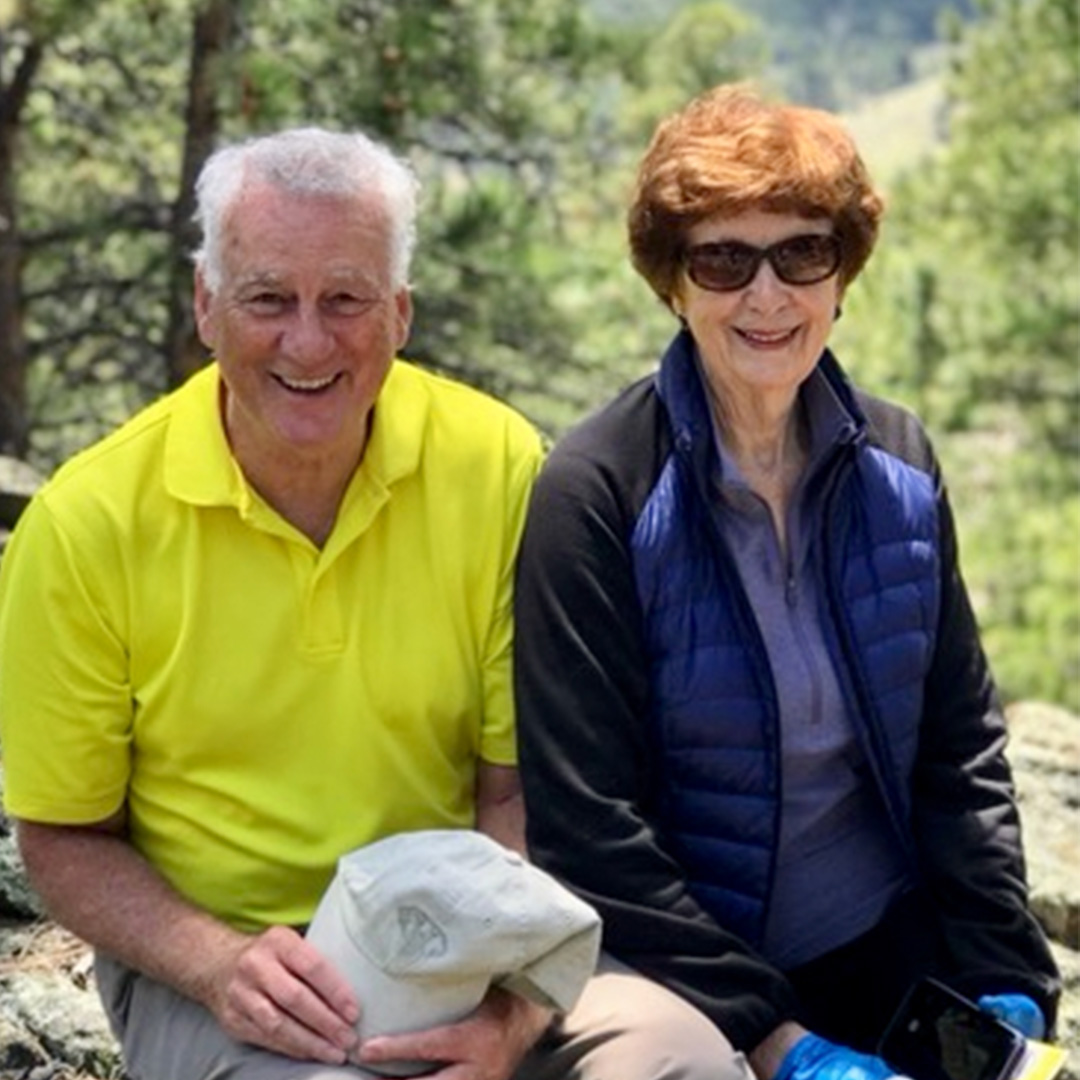 Current photo of Mike and Mimi Glode, pictured sitting on large rocks in an outdoor setting